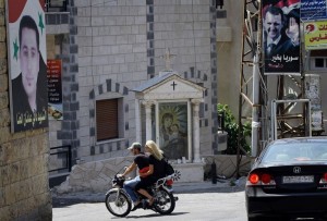 People ride past a Christian shrine and posters of President Bashar al-Assad and a martyr named Dani Adnan al-Hanna in Marmarita in Syria, on August 19, 2013